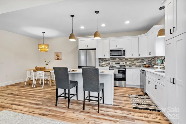 kitchen featuring appliances with stainless steel finishes, white cabinets, a kitchen island, decorative backsplash, and decorative light fixtures