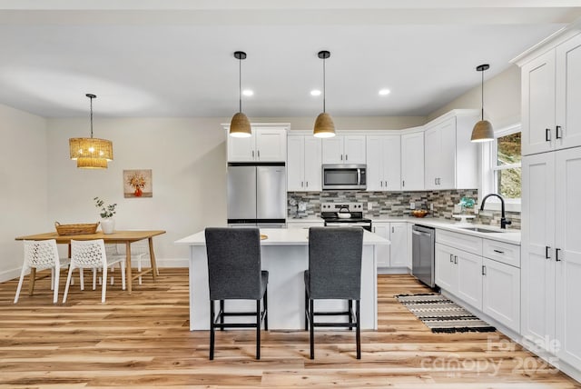 kitchen featuring sink, a center island, hanging light fixtures, stainless steel appliances, and white cabinets