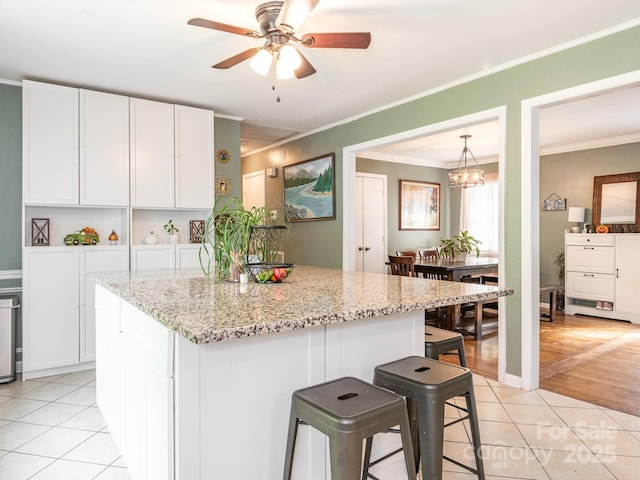 kitchen featuring white cabinetry, a breakfast bar area, light tile patterned floors, and light stone counters