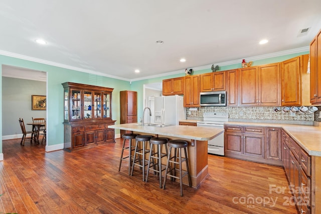 kitchen with a kitchen bar, tasteful backsplash, a center island with sink, ornamental molding, and white appliances