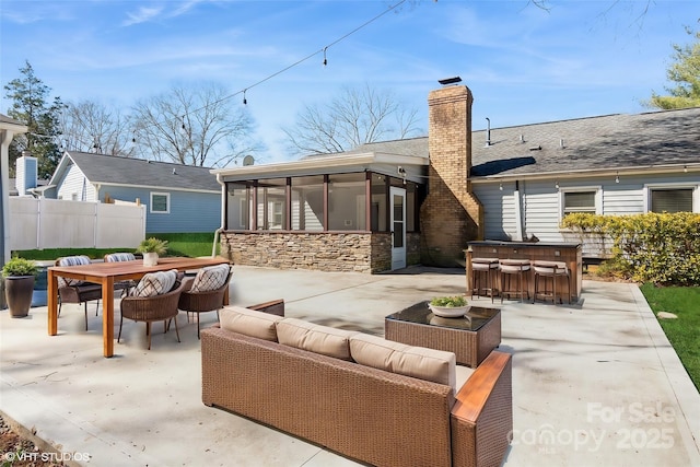 back of property featuring an outdoor living space, a sunroom, outdoor dry bar, stone siding, and a patio area