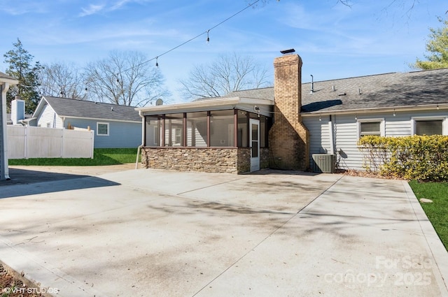 rear view of property with central AC, fence, a sunroom, stone siding, and a chimney