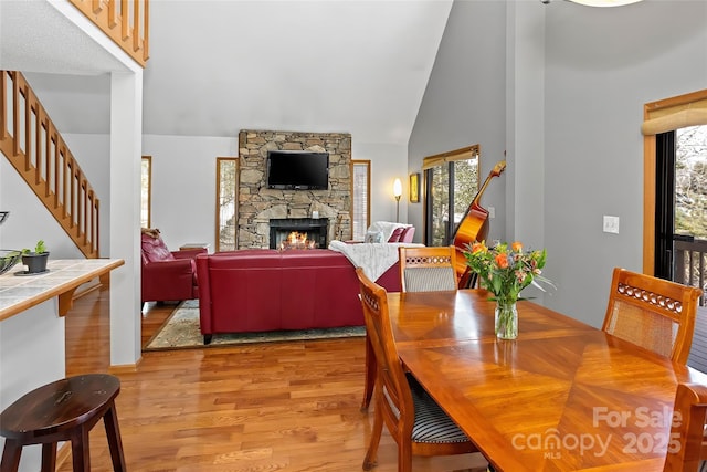 dining area featuring a healthy amount of sunlight, a stone fireplace, high vaulted ceiling, and light wood-type flooring