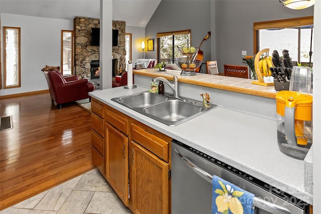 kitchen with a fireplace, lofted ceiling, sink, stainless steel dishwasher, and light hardwood / wood-style floors