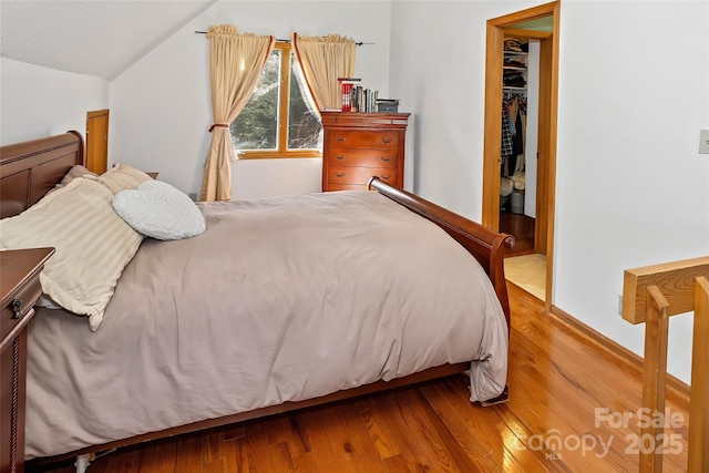 bedroom featuring lofted ceiling, hardwood / wood-style flooring, a walk in closet, and a closet