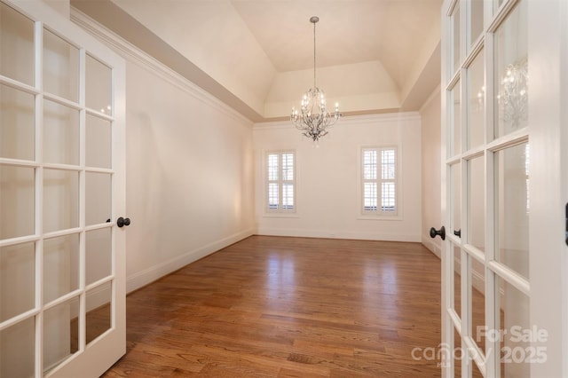 empty room with wood-type flooring, a tray ceiling, an inviting chandelier, and french doors