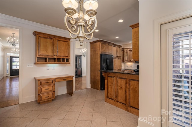 kitchen featuring crown molding, black fridge, dark stone countertops, light tile patterned floors, and a notable chandelier