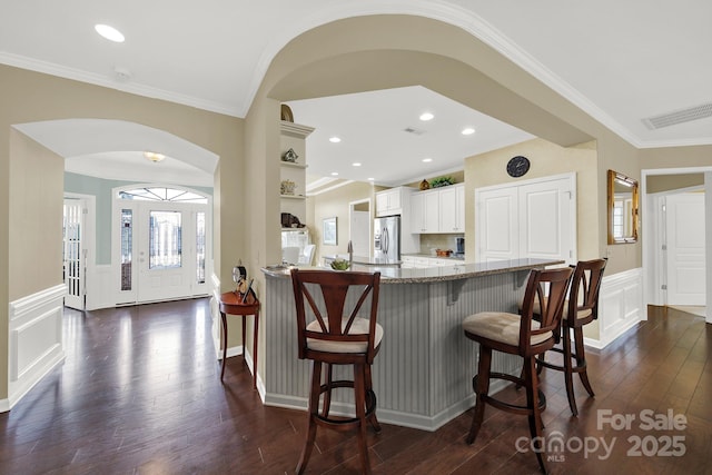 kitchen with crown molding, a breakfast bar, dark hardwood / wood-style floors, white cabinets, and stainless steel fridge with ice dispenser