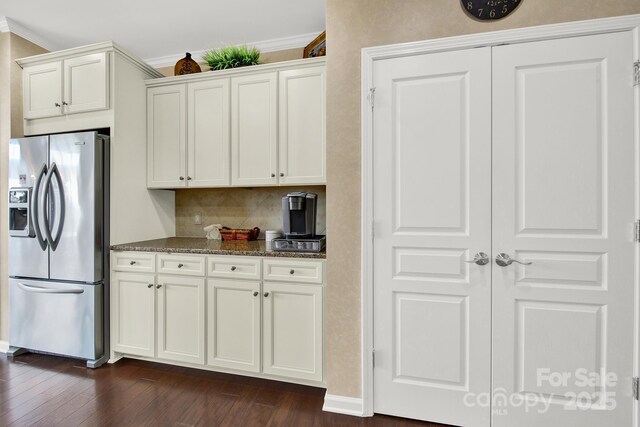 kitchen with stainless steel refrigerator with ice dispenser, ornamental molding, dark stone countertops, and decorative backsplash