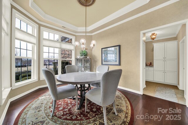 dining room featuring a raised ceiling, ornamental molding, dark wood-type flooring, and an inviting chandelier