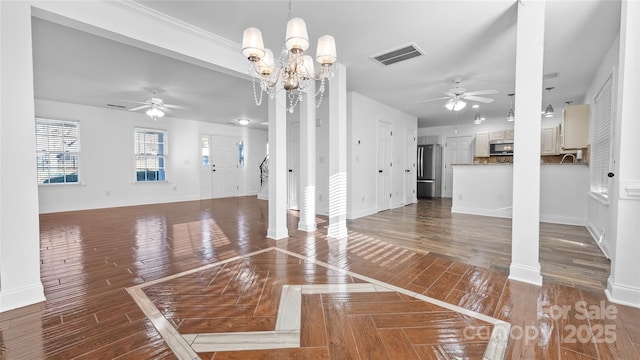 unfurnished living room featuring ceiling fan with notable chandelier and ornate columns