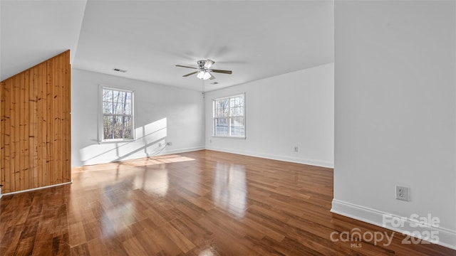 unfurnished room with wood-type flooring, wooden walls, and ceiling fan