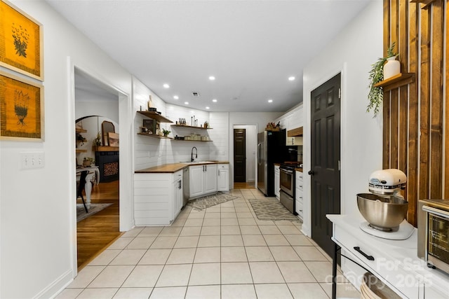 kitchen with sink, stainless steel appliances, white cabinets, light tile patterned flooring, and wood counters