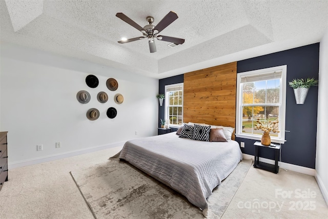 bedroom featuring wooden walls, light colored carpet, a raised ceiling, and ceiling fan