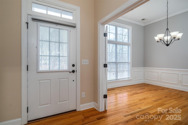 doorway with an inviting chandelier, ornamental molding, and light hardwood / wood-style flooring