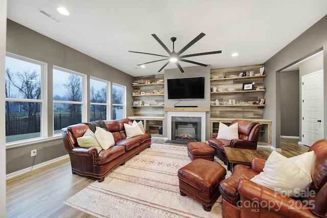 living room featuring light wood-type flooring, built in shelves, and ceiling fan