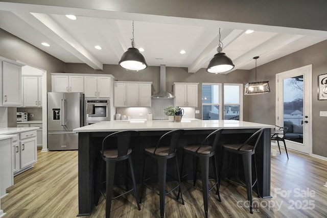 kitchen featuring wall chimney range hood, appliances with stainless steel finishes, white cabinetry, and a large island