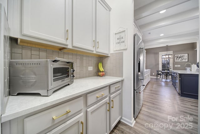 kitchen with tasteful backsplash, hanging light fixtures, light stone countertops, white cabinets, and stainless steel fridge