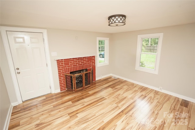 unfurnished living room with a fireplace, a healthy amount of sunlight, and light wood-type flooring