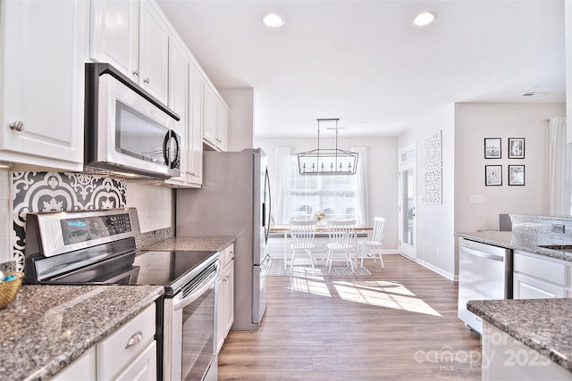 kitchen with stone countertops, tasteful backsplash, white cabinetry, hanging light fixtures, and stainless steel appliances