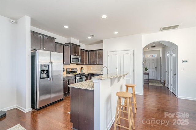 kitchen featuring a breakfast bar, tasteful backsplash, appliances with stainless steel finishes, light stone countertops, and a kitchen island with sink