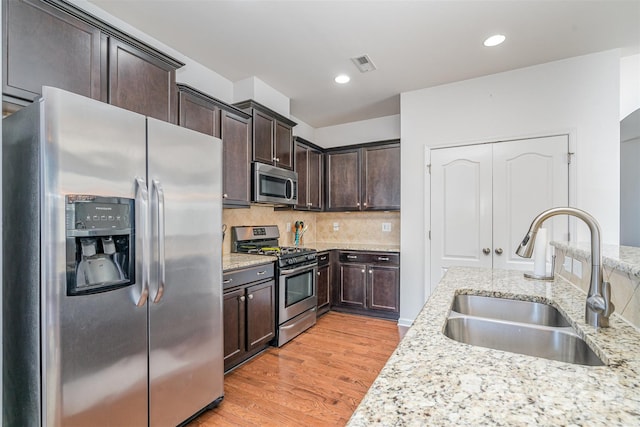 kitchen featuring sink, appliances with stainless steel finishes, light stone counters, decorative backsplash, and light wood-type flooring