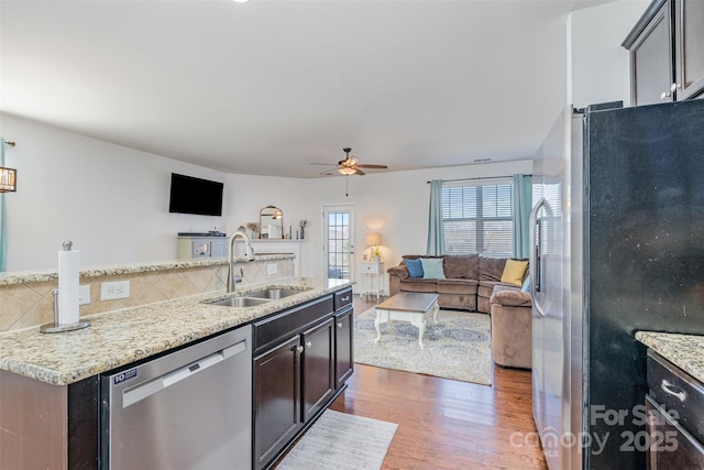 kitchen featuring dark brown cabinetry, sink, stainless steel appliances, light stone countertops, and hardwood / wood-style floors