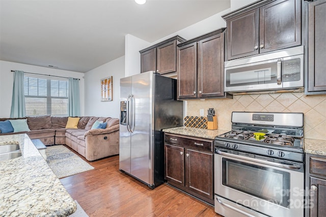 kitchen featuring appliances with stainless steel finishes, light stone counters, dark brown cabinetry, and light hardwood / wood-style floors