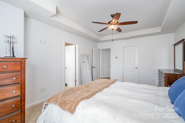 bedroom featuring a raised ceiling, light colored carpet, and ceiling fan