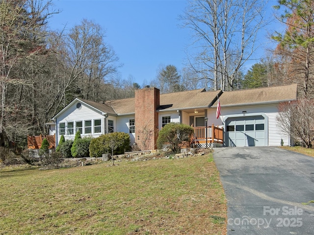 ranch-style home featuring an attached garage, driveway, a chimney, and a front yard