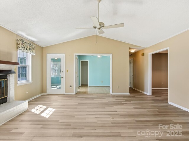 unfurnished living room with lofted ceiling, light wood-type flooring, a textured ceiling, and a brick fireplace