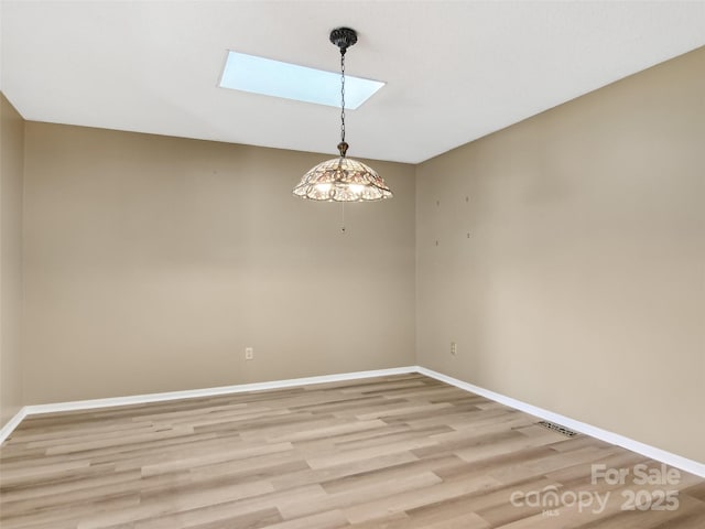 empty room with a skylight, baseboards, and light wood-style floors