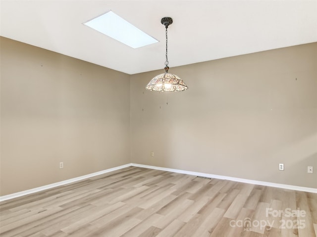 empty room featuring a skylight, visible vents, baseboards, and light wood finished floors