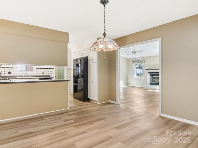 unfurnished dining area featuring a fireplace with raised hearth, ceiling fan, light wood-style flooring, and baseboards