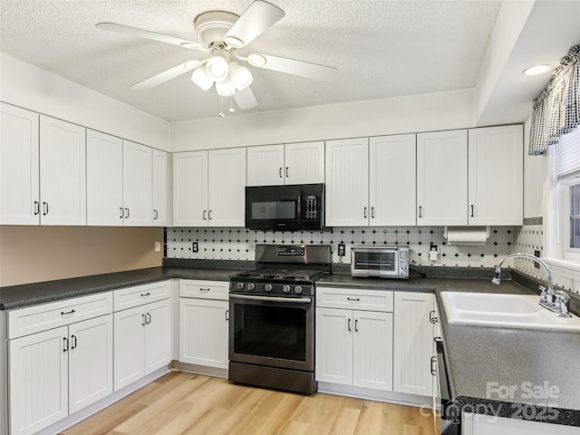 kitchen featuring a toaster, stainless steel gas range oven, white cabinets, black microwave, and a sink