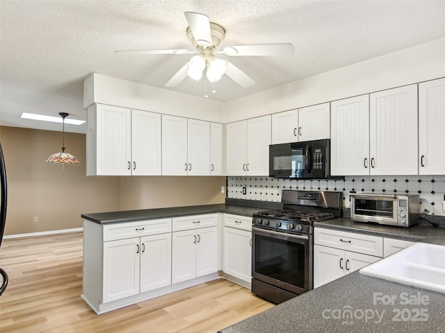 kitchen featuring a toaster, stainless steel gas range oven, dark countertops, light wood-style floors, and black microwave