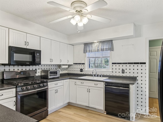 kitchen with dark countertops, a sink, light wood-style flooring, and black appliances