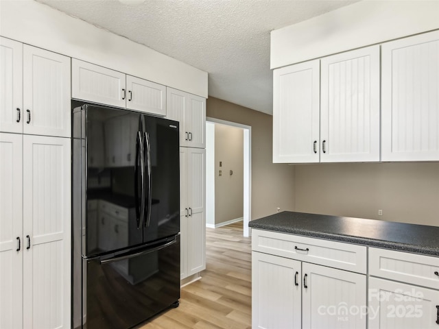 kitchen with a textured ceiling, white cabinetry, light wood-style floors, freestanding refrigerator, and dark countertops