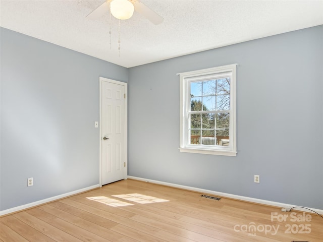 empty room featuring a textured ceiling, ceiling fan, wood finished floors, visible vents, and baseboards