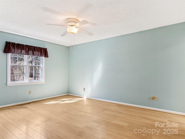 spare room with ceiling fan, a textured ceiling, wood finished floors, visible vents, and baseboards