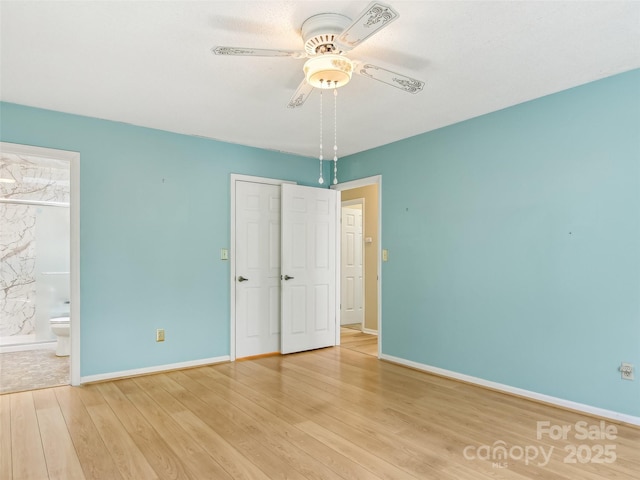 unfurnished bedroom featuring ensuite bathroom, ceiling fan, wood finished floors, baseboards, and a closet