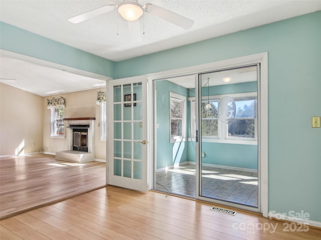 doorway featuring a textured ceiling, ceiling fan, wood finished floors, visible vents, and a glass covered fireplace