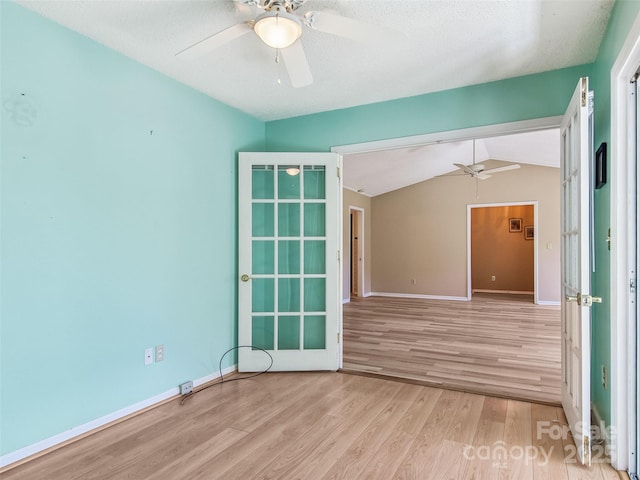 spare room with lofted ceiling, light wood-style floors, baseboards, and a ceiling fan