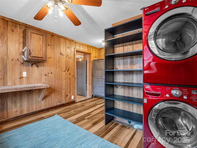 laundry area featuring light hardwood / wood-style flooring, wood walls, ceiling fan, and stacked washer / dryer