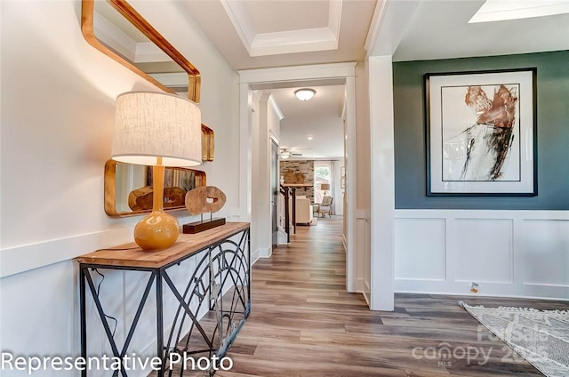 corridor with ornamental molding, wainscoting, a decorative wall, and wood finished floors