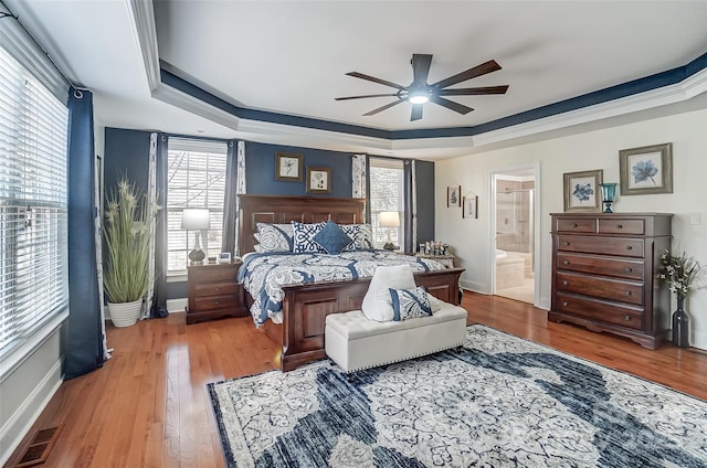 bedroom featuring ceiling fan, connected bathroom, a tray ceiling, and hardwood / wood-style floors