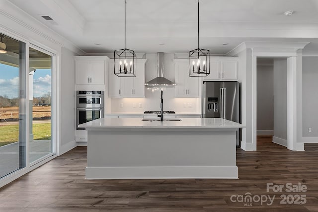 kitchen with white cabinetry, an island with sink, hanging light fixtures, stainless steel appliances, and wall chimney exhaust hood