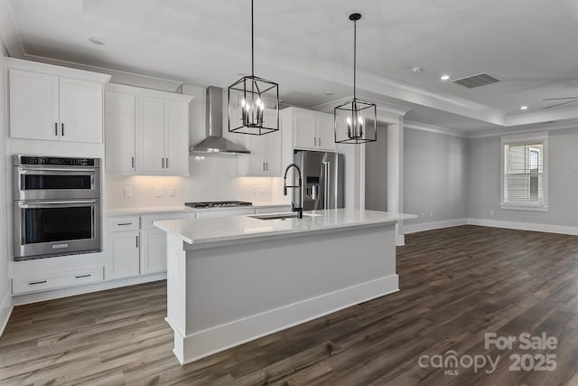 kitchen with wall chimney exhaust hood, sink, hanging light fixtures, a center island with sink, and stainless steel appliances