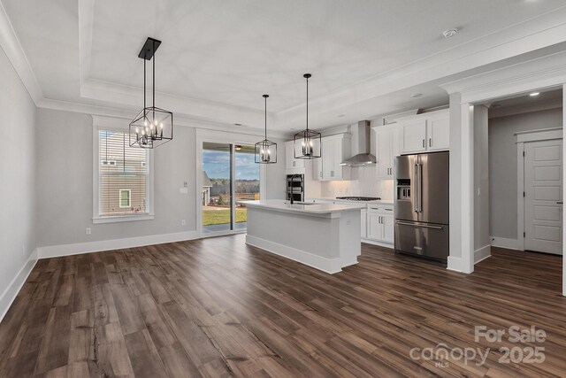 kitchen with pendant lighting, white cabinetry, high end refrigerator, a center island with sink, and wall chimney range hood