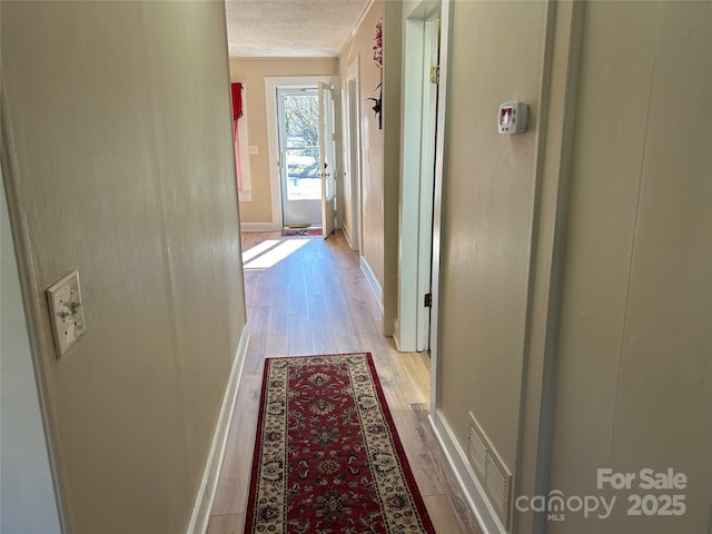 hall with a textured ceiling and light hardwood / wood-style floors